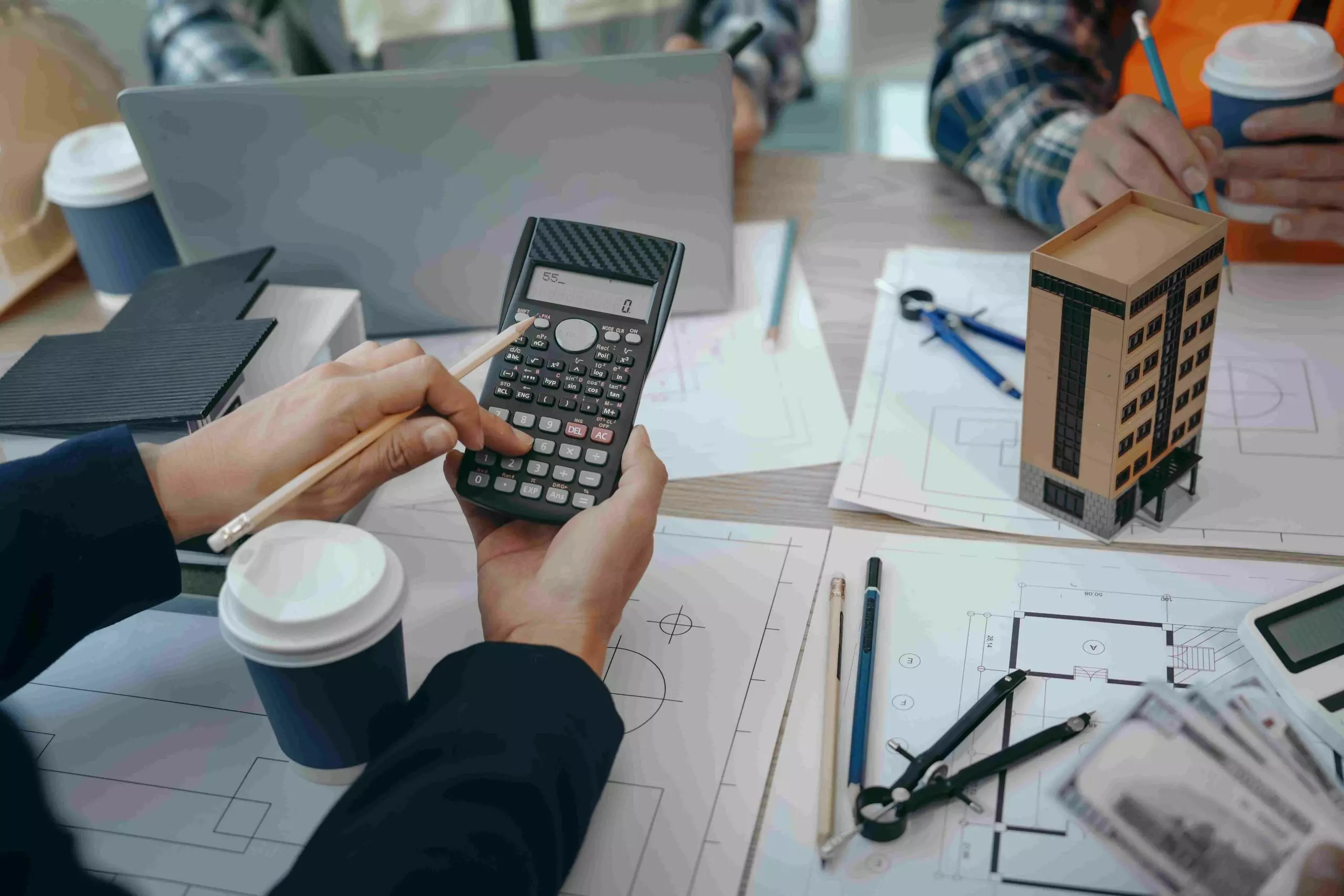 Personne utilisant une calculatrice et des plans architecturaux.