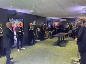 Groupe de personnes dans une salle de réunion, certains debout, d'autres assis, avec un homme parlant dans un microphone.
